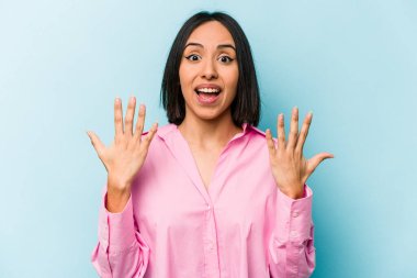 Mavi arka planda izole edilmiş genç İspanyol kadın on numarayı elleriyle gösteriyor..
