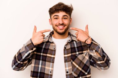 Beyaz arka planda izole edilmiş genç İspanyol adam gülümsüyor, parmaklarını ağıza doğrultuyor..