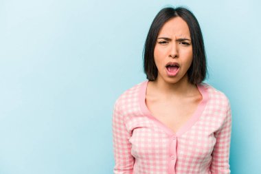 Mavi arka planda izole edilmiş genç İspanyol kadın çok kızgın, öfkeli, hayal kırıklığına uğramış.