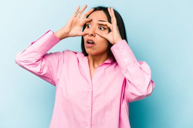 Mavi arka planda izole edilmiş genç İspanyol kadın bir başarı fırsatı bulmak için gözlerini açık tutuyor..