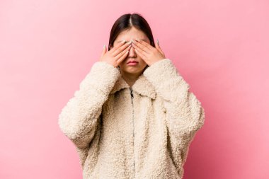 Pembe arka planda izole edilmiş genç Çinli kadın elleriyle gözlerini kapatmaktan korkuyor..