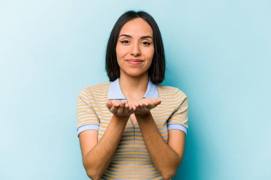 Mavi arka planda izole edilmiş genç İspanyol kadın elinde avuç içi bir şeyle kameraya sunuyor..