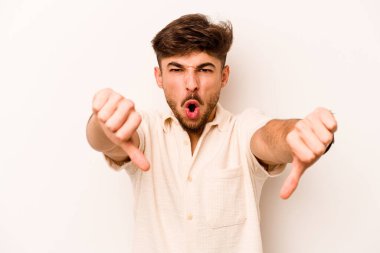 Beyaz arka planda izole edilmiş genç İspanyol adam baş parmağını aşağı gösteriyor ve hoşlanmadığını ifade ediyor..