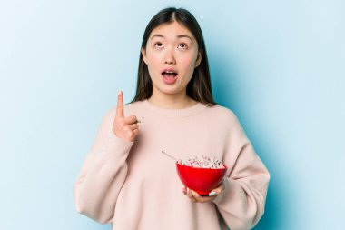 Genç Asyalı bir kadın elinde bir kase mısır gevreği tutuyordu. Mavi arka planda, ağzı açık, üst tarafı işaret ediyordu..