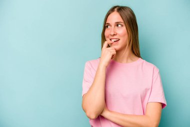 Mavi arka planda izole edilmiş genç beyaz kadın rahatça fotokopi odasına bakan bir şey düşünüyor..
