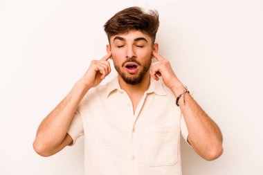 Beyaz arka planda izole edilmiş, kulakları parmaklarla kaplayan, stresli ve çaresiz genç bir İspanyol..
