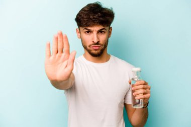 Beyaz arka planda izole edilmiş bir şişe su tutan İspanyol genç adam elini uzatmış, dur işareti göstererek seni engelliyor..