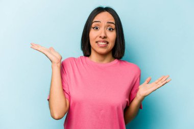 Genç İspanyol kadın mavi arka planda izole edilmiş. Kafası karışmış ve omuz silkiyor. Kopya alanını tutmak için..