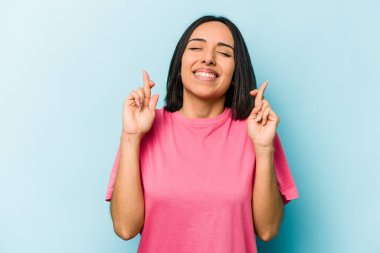 Genç İspanyol kadın mavi arka planda izole edilmiş şans dilemek için şans diliyor.