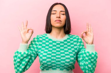 Pembe arka planda izole edilmiş genç İspanyol kadın sıkı çalışma gününden sonra rahatlıyor, yoga yapıyor..