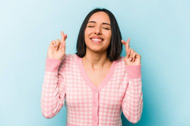 Genç İspanyol kadın mavi arka planda izole edilmiş şans dilemek için şans diliyor.