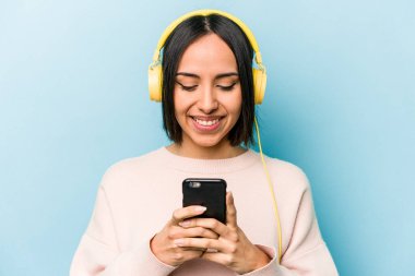 Genç İspanyol kadın mavi arka planda izole edilmiş müzik dinliyor.