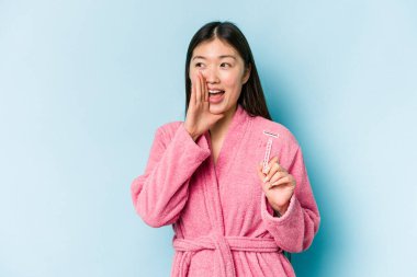 Elinde jilet tutan genç Asyalı kadın mavi arka planda izole edilmiş bağırıyor ve avuç içini açık tutuyor..