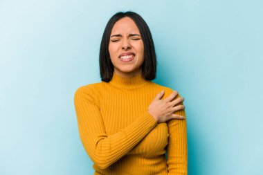 Mavi arka planda izole edilmiş genç İspanyol kadın omuz ağrısı çekiyor..