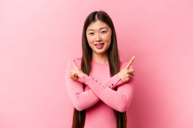 Pembe arka planda izole edilmiş genç Çinli kadın iki seçenek arasında seçim yapmaya çalışıyor..