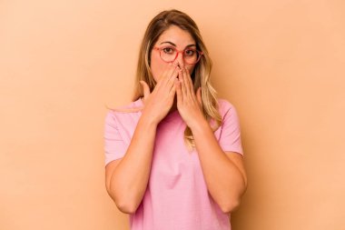Beyazlı genç bir kadın bej arka planda izole edilmiş. Ağzını elleriyle kapatmış..