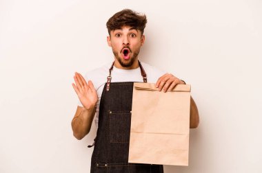 Beyaz arka planda izole edilmiş bir paket taşıyan genç İspanyol tezgahtar şaşırdı ve şok oldu..