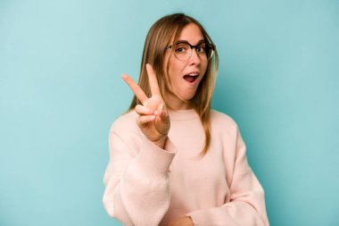 Mavi arka planda izole edilmiş genç beyaz kadın iki numarayı parmaklarıyla gösteriyor..