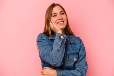 Pembe arka planda izole edilmiş genç beyaz kadın mutlu bir şekilde gülüyor ve ellerini karnının üstünde tutarak eğleniyor..