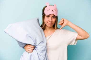Mavi arka planda izole edilmiş pijama giyen, hoşlanmadığı bir hareket gösteren beyaz bir kadın. Anlaşmazlık konsepti.