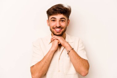 Beyaz arka planda izole edilmiş genç İspanyol adam ellerini çenesinin altında tutuyor ve mutlu bir şekilde yan tarafa bakıyor..