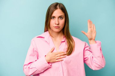 Beyaz bir kadın mavi arka planda izole edilmiş yemin ediyor, elini göğsüne koyuyor..