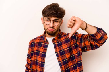Beyaz arka planda izole edilmiş genç İspanyol adam baş parmağını aşağı gösteriyor ve hoşlanmadığını ifade ediyor..