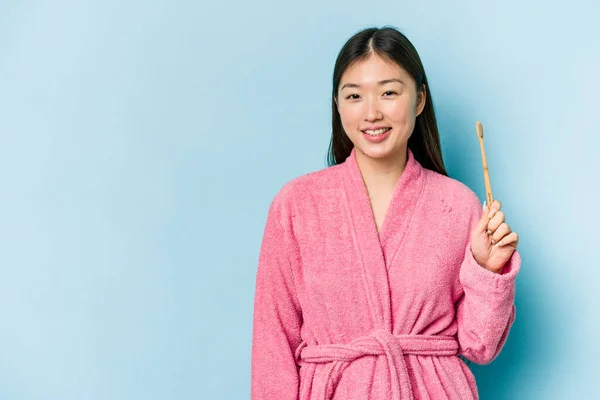年轻的亚洲女人穿着浴衣 用粉红的背景 微笑着 竖起大拇指来刷牙 — 图库照片