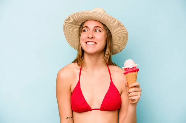 年轻的高加索女人穿着比基尼 拿着用蓝色背景隔开的冰淇淋 梦想着实现自己的目标和目的 — 图库照片