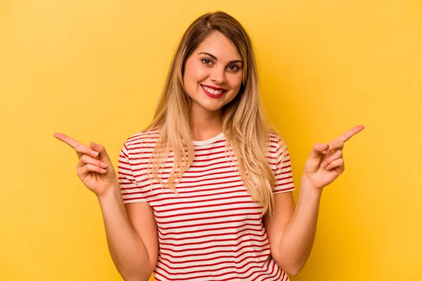 stock image Young caucasian woman isolated on yellow background pointing to different copy spaces, choosing one of them, showing with finger.