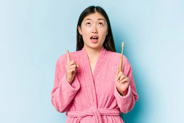 年轻的亚洲女人穿着浴衣刷牙 带着粉色背景 上身朝上 张开嘴 — 图库照片