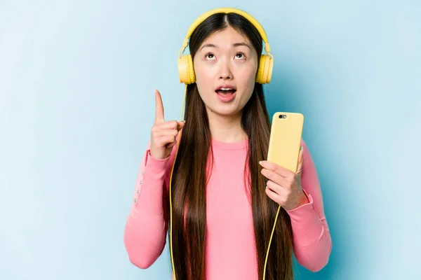 Jovem Mulher Asiática Ouvindo Música Isolada Fundo Azul Apontando Cabeça — Fotografia de Stock