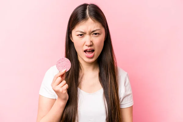 年轻的亚洲女人拿着用粉红背景隔离起来的面部海绵尖叫着 非常愤怒和咄咄逼人 — 图库照片