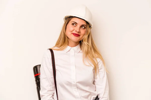 Young architect woman with helmet and holding blueprints isolated on white background dreaming of achieving goals and purposes