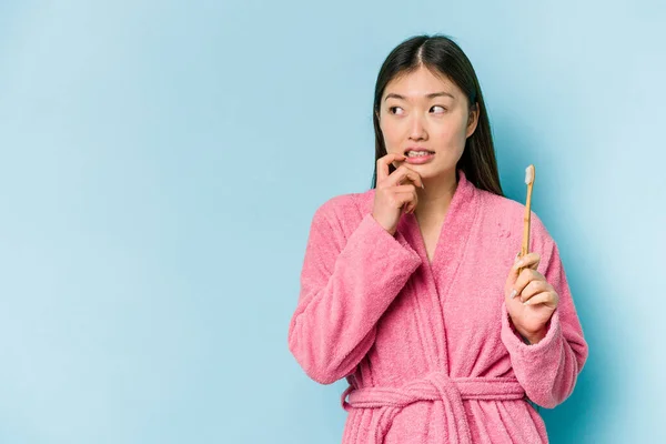 年轻的亚洲女人穿着浴衣刷牙 背景是粉色的 很轻松地想象着有什么东西在看复制的空间 — 图库照片