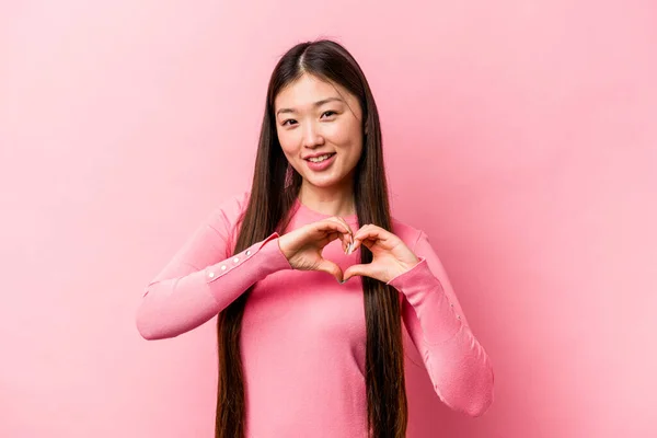 年轻的中国女人在粉红的背景上被隔离 面带微笑 双手呈心形 — 图库照片