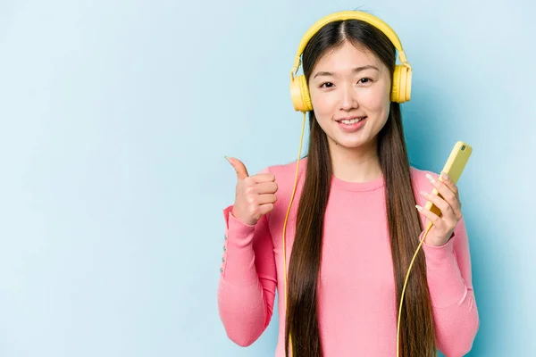 Jovem Mulher Asiática Ouvindo Música Isolada Fundo Azul Sorrindo Levantando — Fotografia de Stock