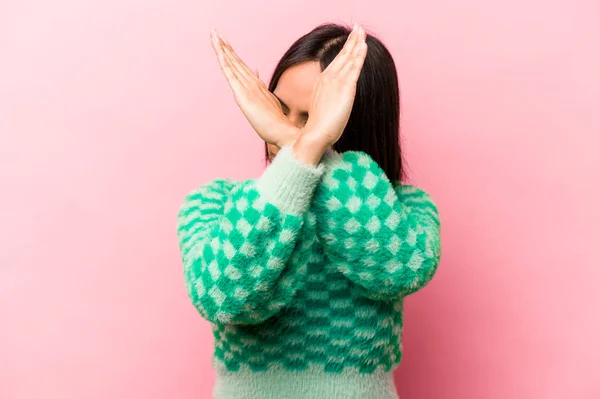 Young hispanic woman isolated on pink background keeping two arms crossed, denial concept.