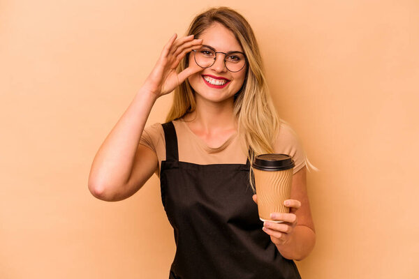 Restaurant waiter caucasian woman holding a take away coffee isolated on beige background excited keeping ok gesture on eye.
