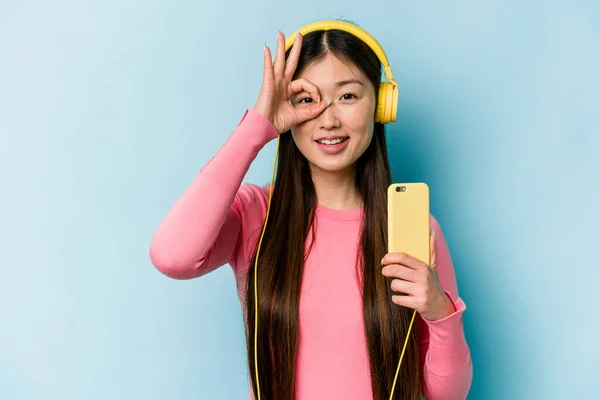Jovem Mulher Asiática Ouvindo Música Isolada Fundo Azul Animado Mantendo — Fotografia de Stock