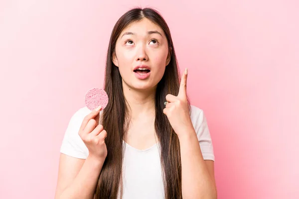 年轻的亚洲女人 用粉红的背景把脸海绵隔离起来 指向上方 张着嘴 — 图库照片