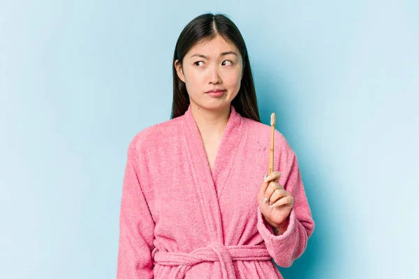 年轻的亚洲女人穿着浴衣刷牙 背景粉红 感到困惑 怀疑和不确定 — 图库照片
