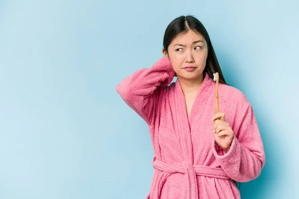 年轻的亚洲女人穿着浴衣 用粉色背景隔离的刷牙 后脑勺接触 思考着 做出选择 — 图库照片