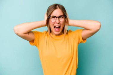 Kafkasyalı genç bir kadın mavi arka planda izole edilmiş kulakları kulaklarıyla kapatıyor çok fazla ses duymamaya çalışıyor..