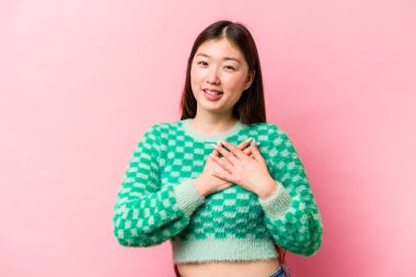 Pembe arka planda izole edilmiş genç Çinli bir kadın, dostane bir ifadeye sahip, avuçlarını göğsüne bastırıyor. Aşk konsepti.