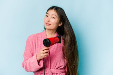 Mavi arka planda saç kurutan Asyalı genç kadın.