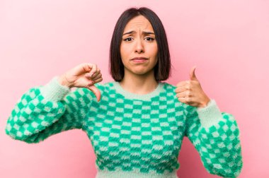 Pembe arka planda izole edilmiş genç İspanyol kadın baş parmağını kaldırıyor, zor seçim konsepti.