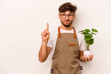 Genç bahçıvan İspanyol bir bitki tutuyor. Beyaz arka planda bir numarayı parmağıyla gösteriyor..