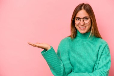 Pembe arka planda izole edilmiş genç beyaz kadın bir avuç içinde fotokopi alanı ve belinde bir el daha gösteriyor..