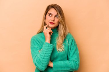 Beyaz tenli genç bir kadın, bej arka planda izole edilmiş, bir strateji tasarlıyor, bir iş hayatının nasıl olacağını düşünüyor..